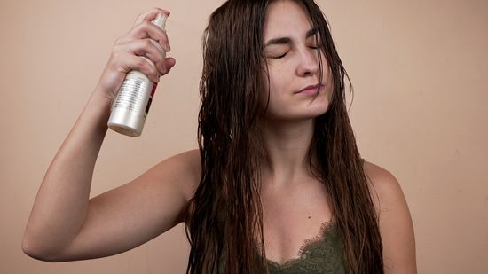 applying heat protectant spray to tousled blond hair