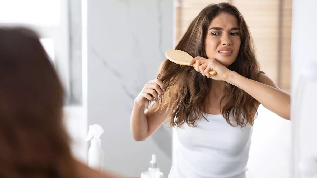 woman struggles with brushing tangled hair in front of mirror