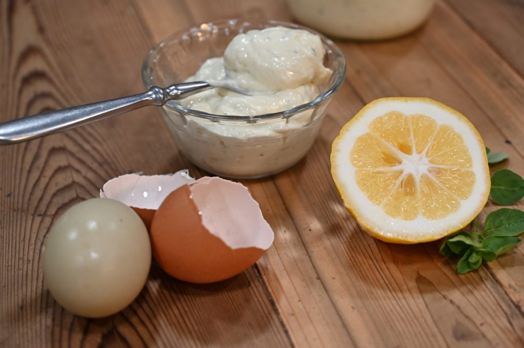 Mayonnaise on spoon with lemon and eggs in the background