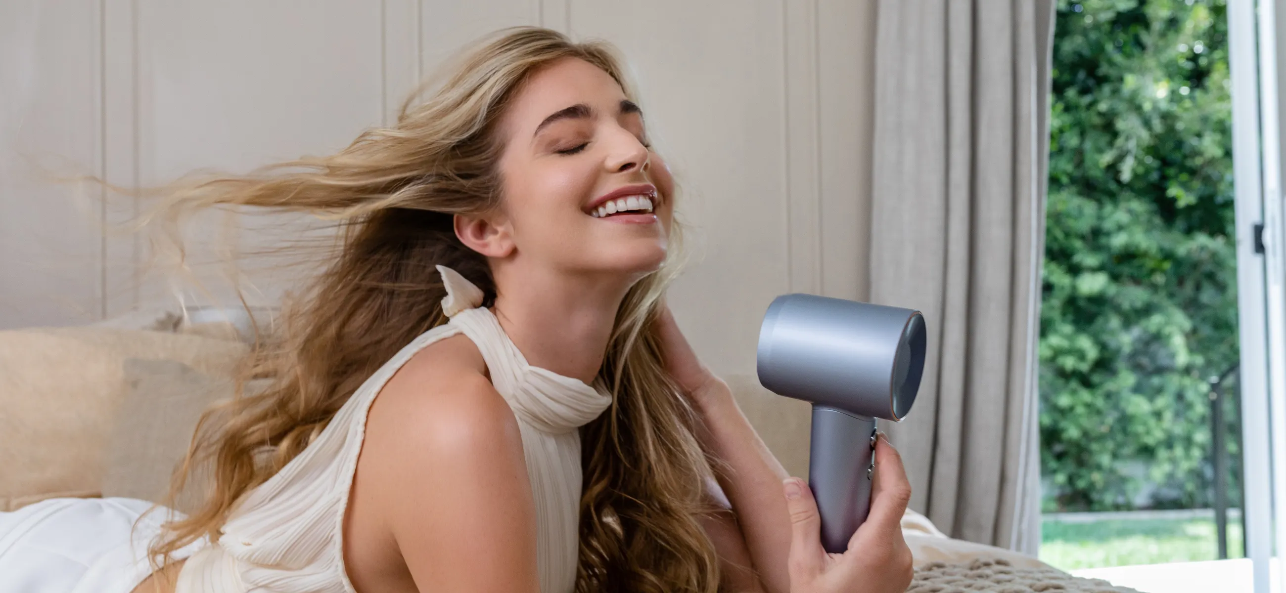 Woman drying her wavy hair with a metallic hair dryer