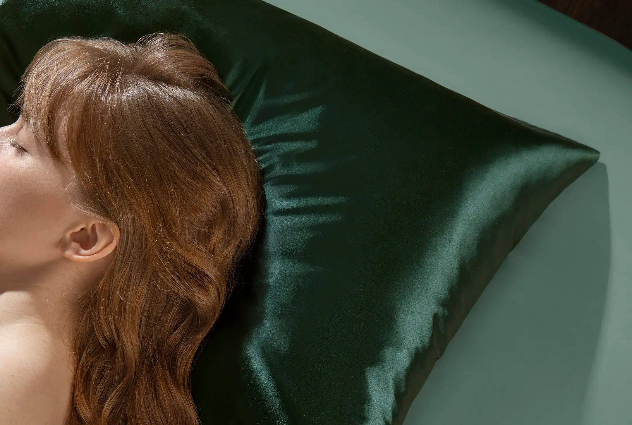 Woman resting on a green satin pillow, hair sprawled out.