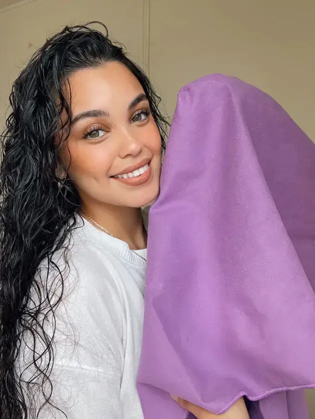 Smiling woman with wet curly hair holding purple towel.