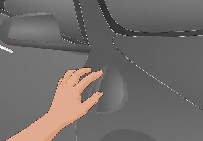 Hand examining a small dent on a car door.