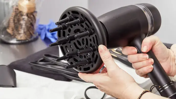 Hair dryer with diffuser attachment being adjusted by hands.
