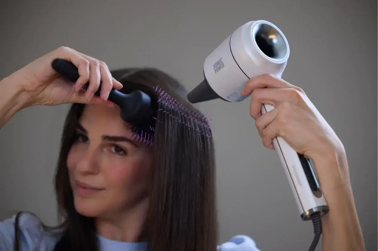 Woman using a modern hair dryer with a brush attachment.