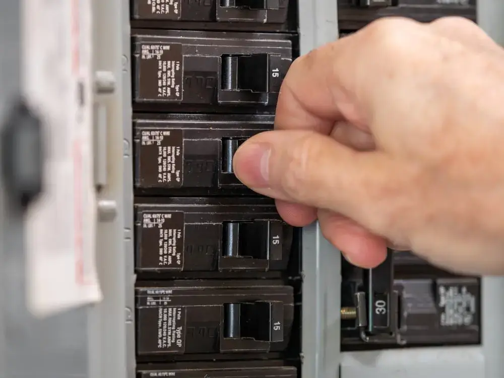 Hand resetting a tripped breaker in an electrical panel.