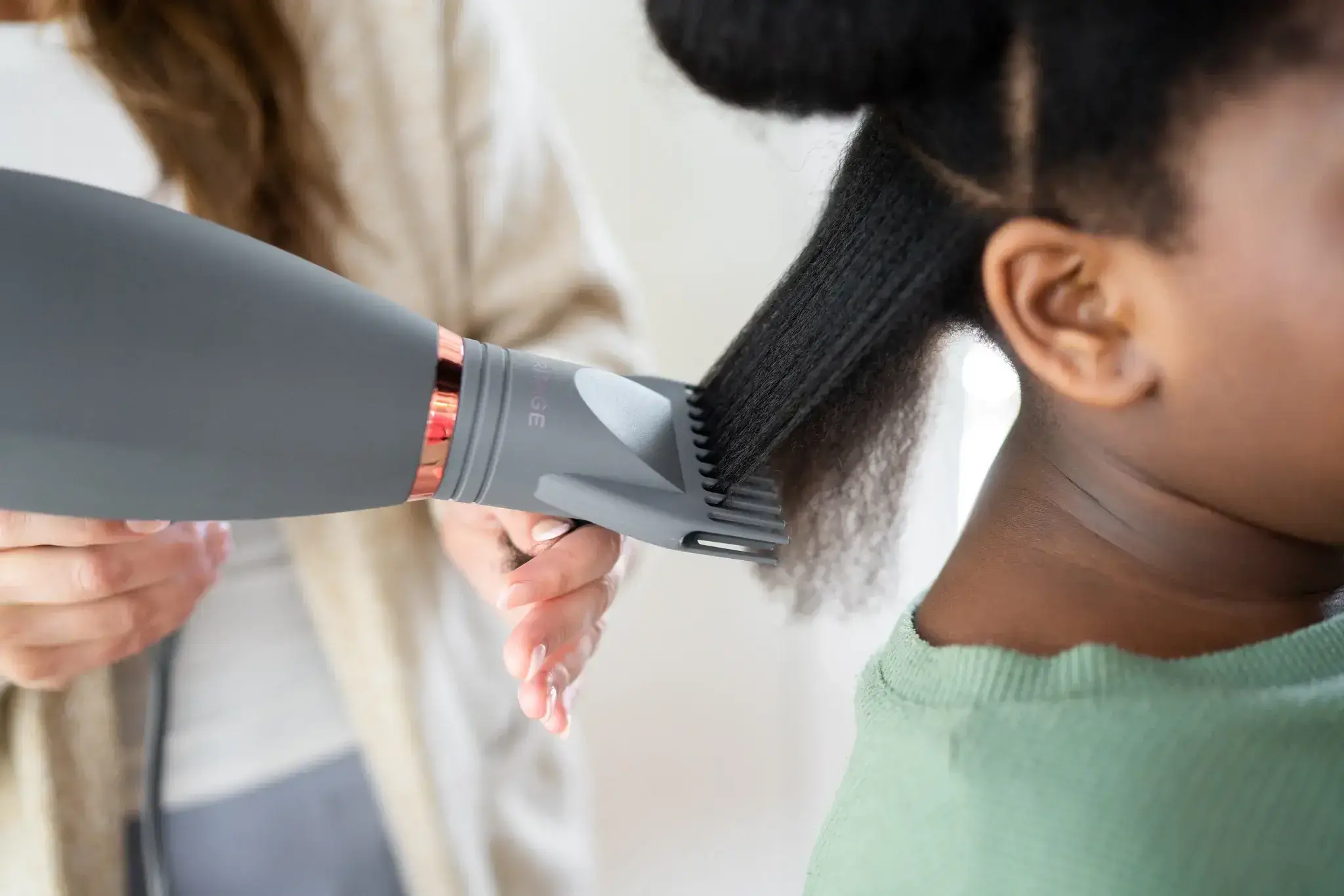 Close-up of a hairdryer with comb attachment on curly hair.