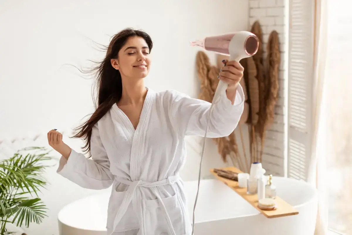 Woman in robe enjoys blow-drying her hair at home.