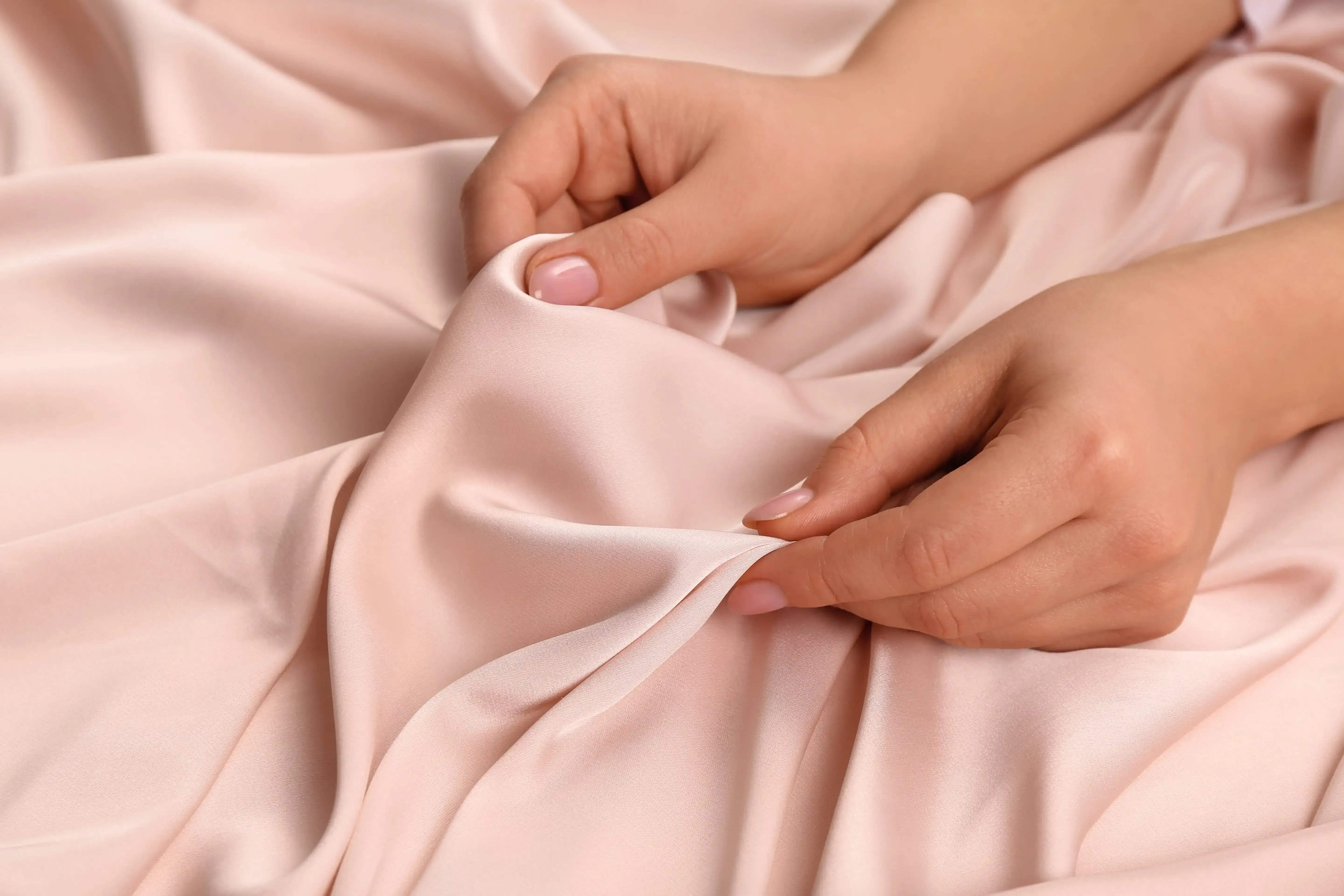 Hands gently examining a piece of satin fabric.