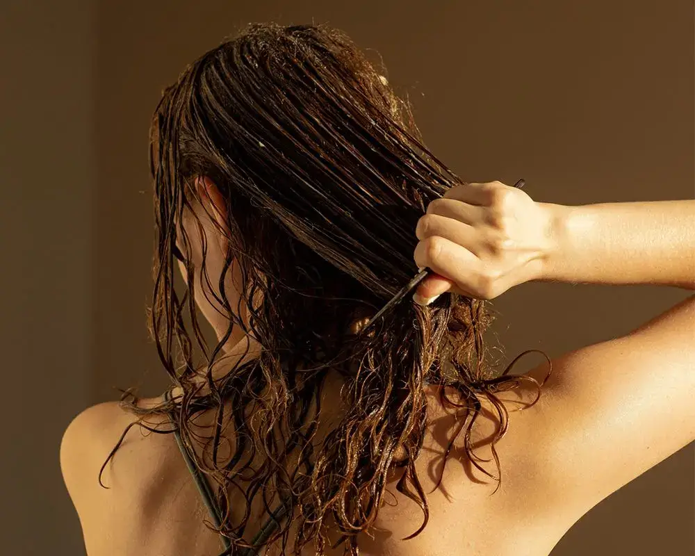 Woman combing through wet, tangled hair.