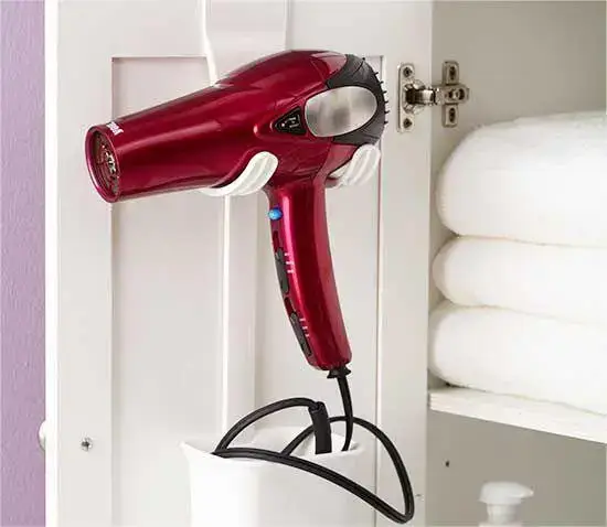 Red hair dryer hanging on cabinet door with cord holder.