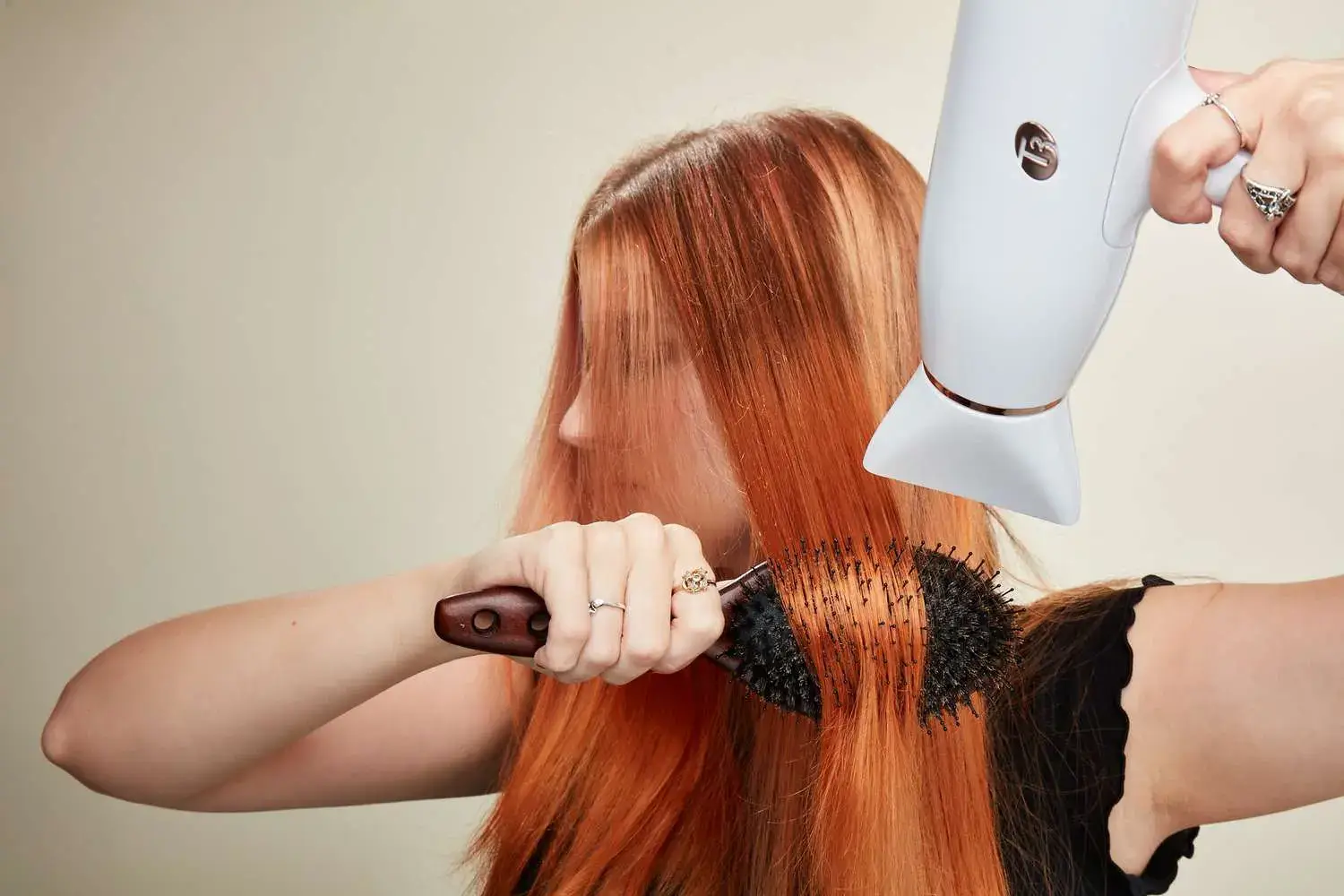Person blow-drying red hair with round brush.