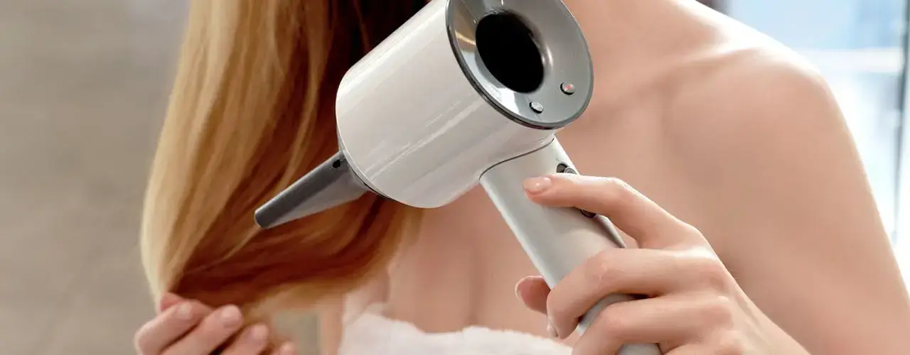 Person drying long blonde hair with a stylish white dryer.