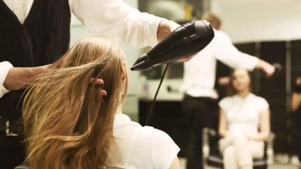 Stylist blow-drying a woman's long blonde hair in salon.