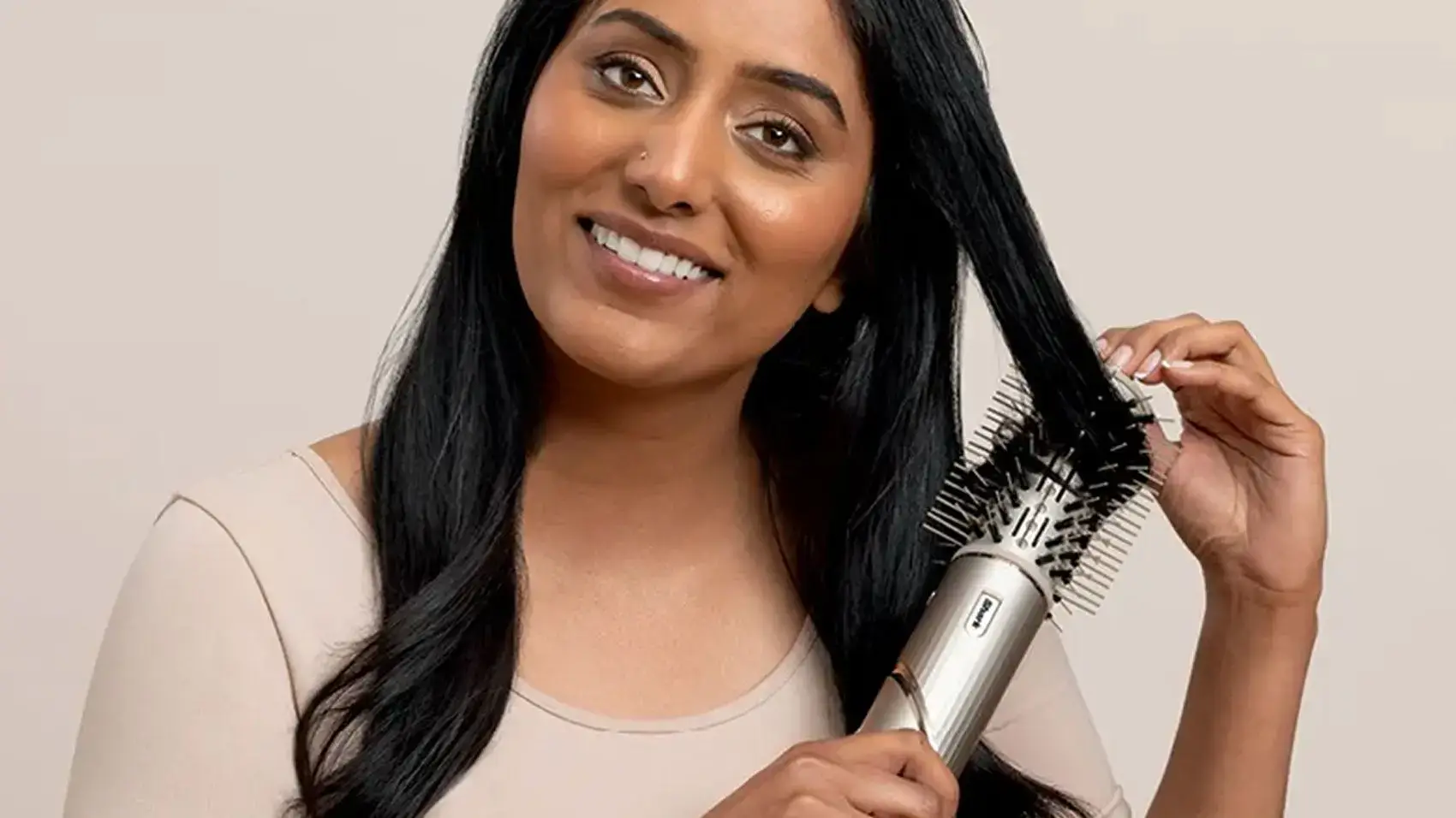 Woman smiling, using a hair dryer brush on her hair.