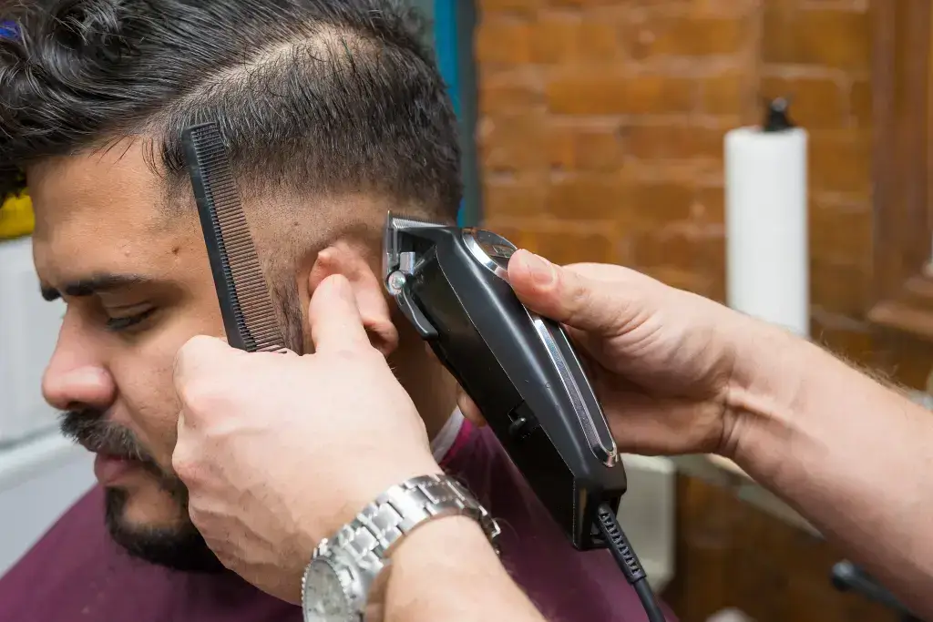 Barber using clippers and comb on a man's haircut.