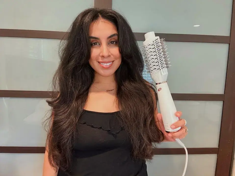 Smiling woman holding a hair dryer brush in salon.