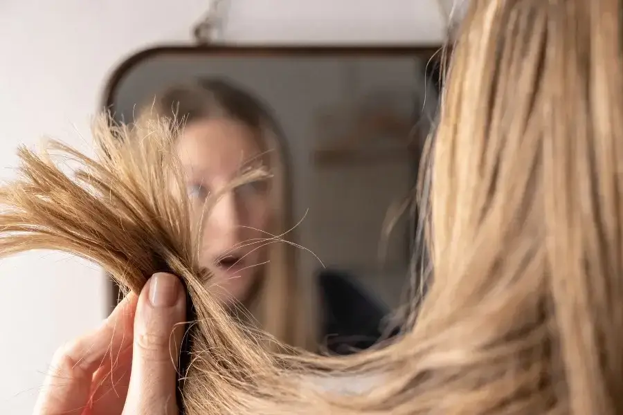 Person inspecting split ends, indicating hair damage.