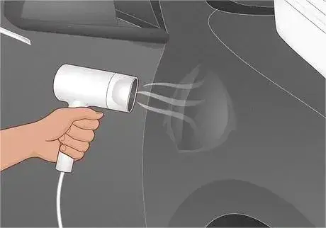 Hair dryer blowing hot air onto a car dent.