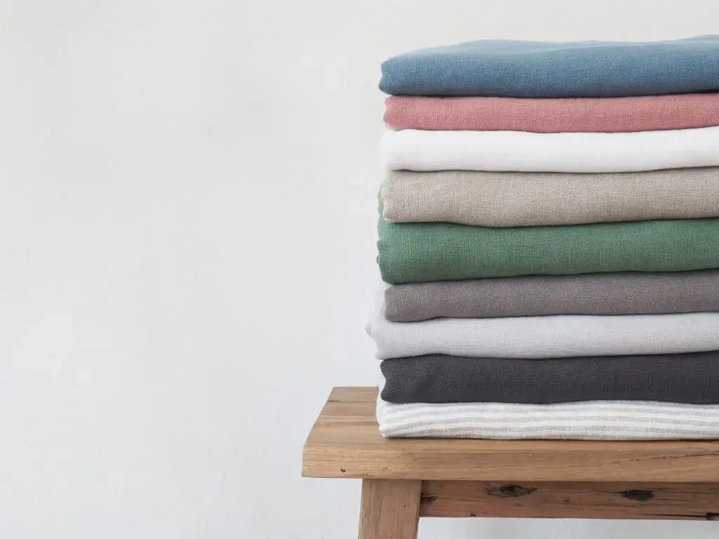 Neatly folded stack of colorful shirts on a wooden bench.