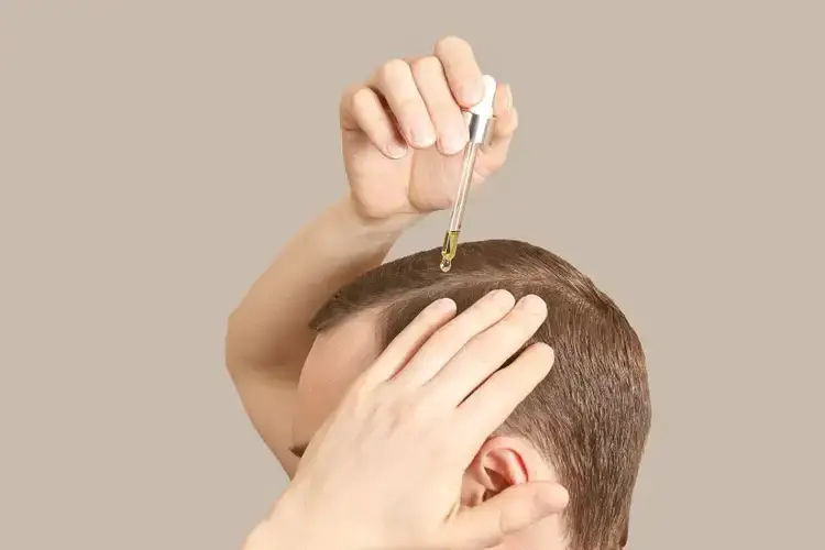 Applying hair oil with dropper on scalp.