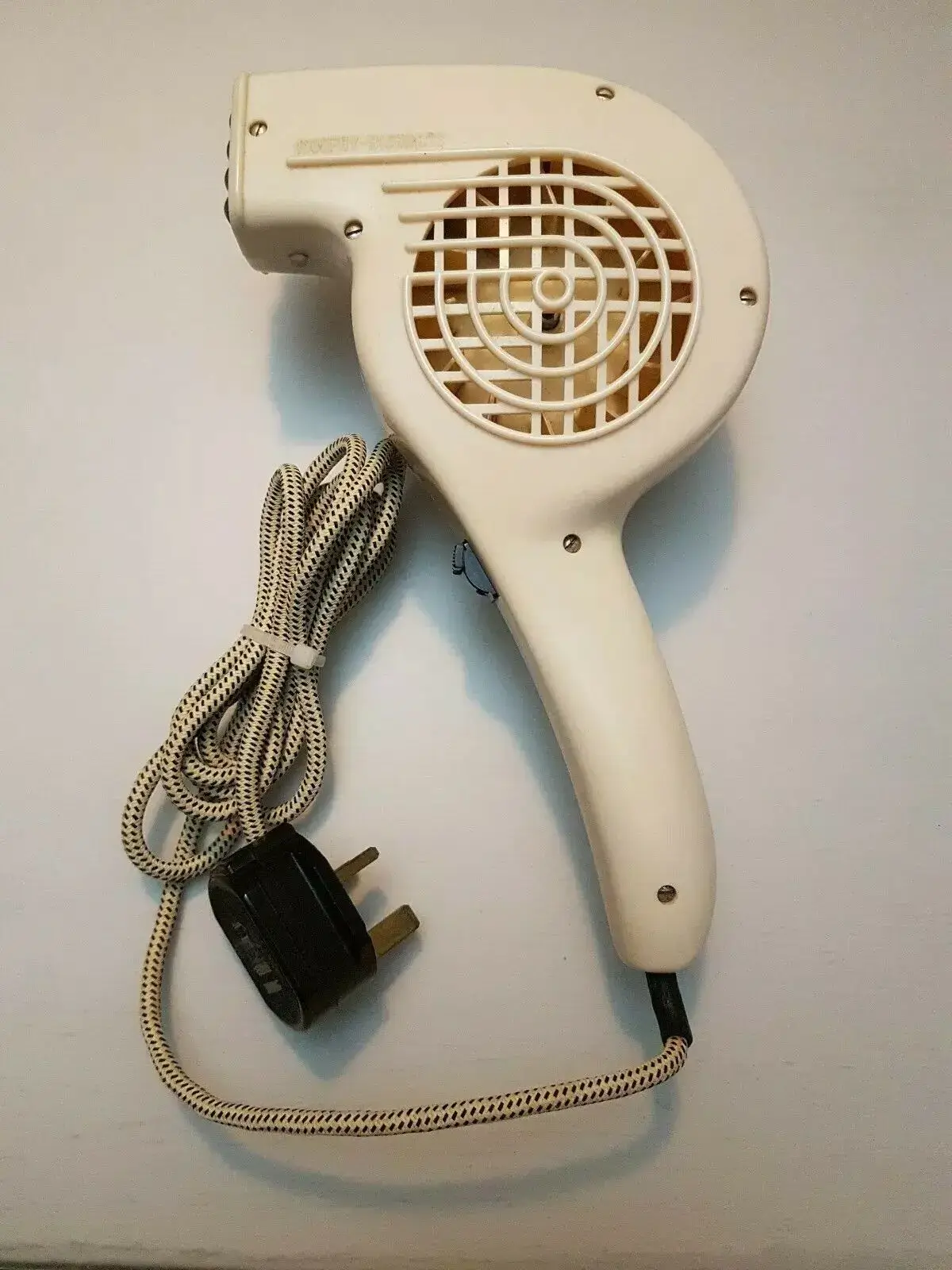 Vintage hair dryer with woven cord on a table.