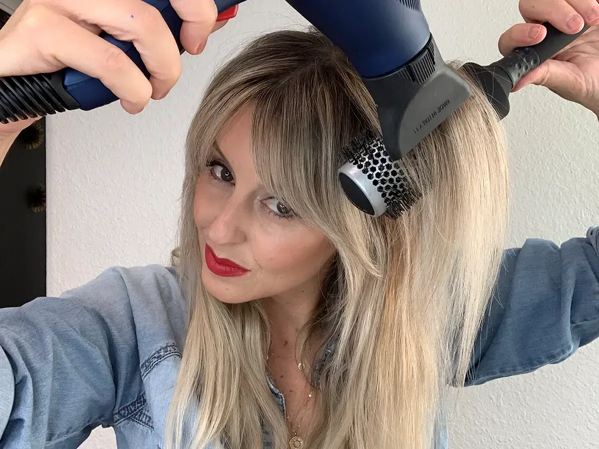 Woman using hair dryer with round brush attachment.