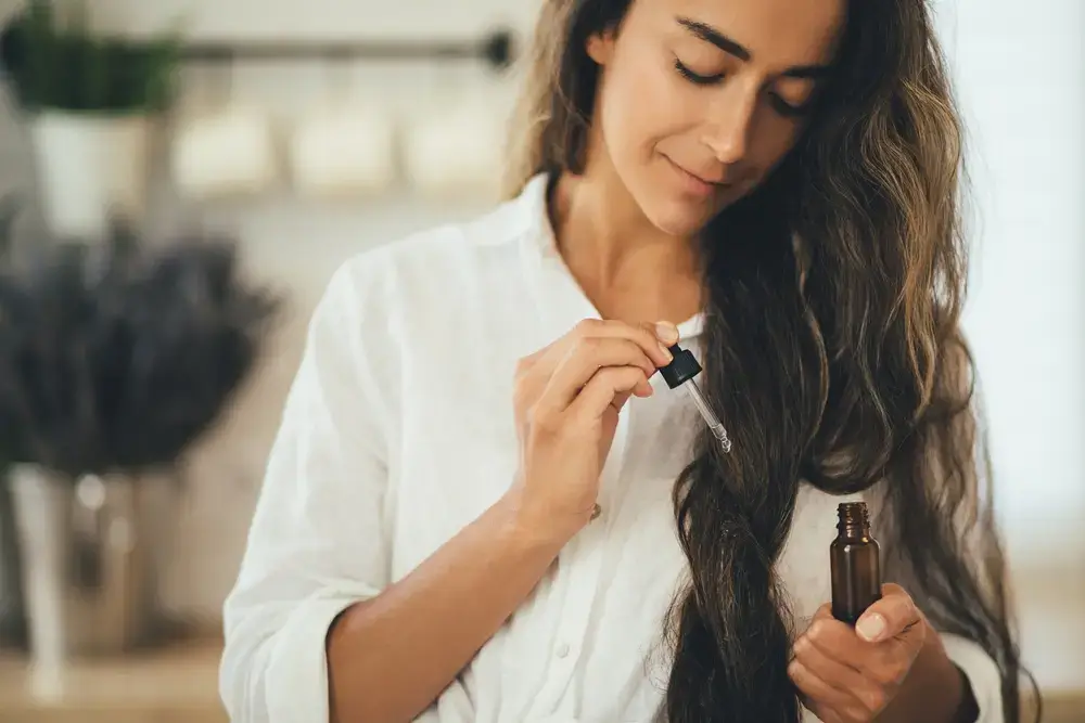 Woman applying oil treatment to her long, wavy hair.