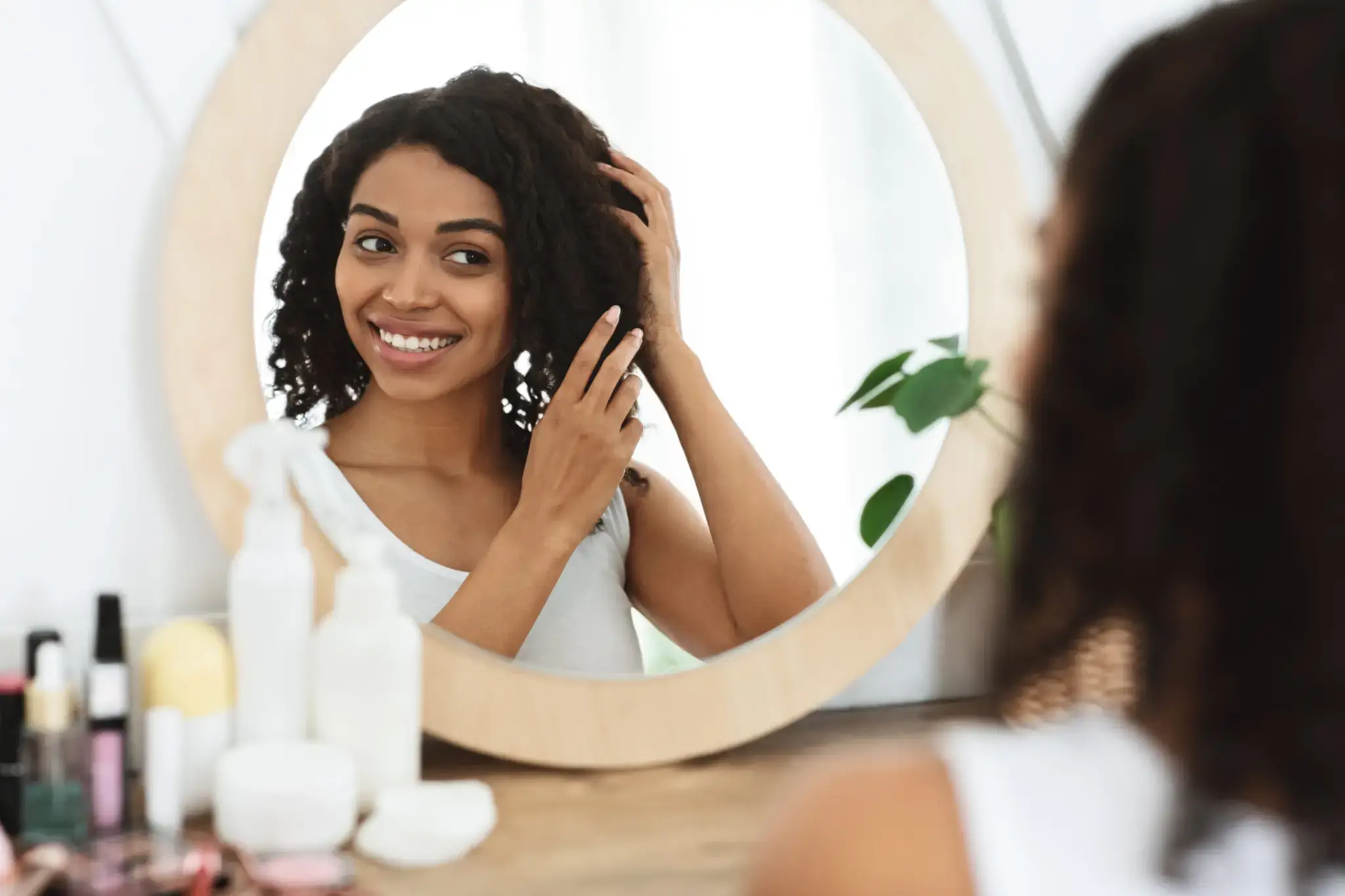 Woman admiring her curly hair in a circular mirror.