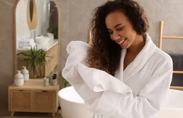 Happy woman drying her curly hair with a white towel.