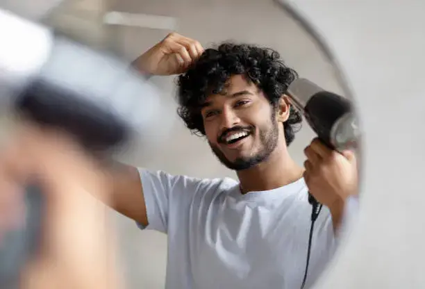 Man happily using a hair dryer, looking in mirror.