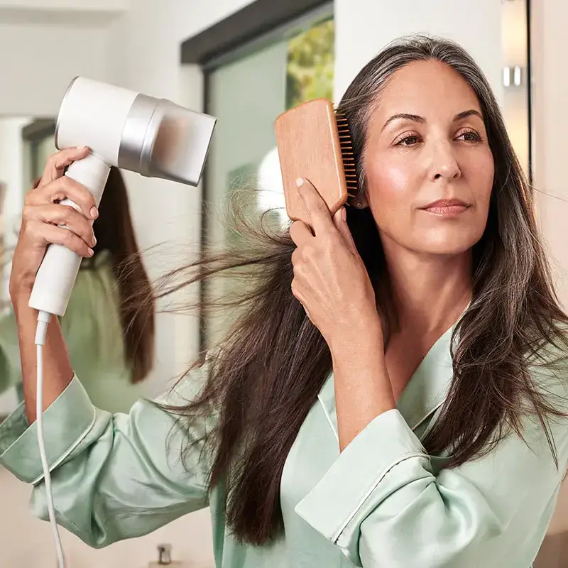 Woman blow-drying her long hair with a hair dryer with a concentrator nozzles