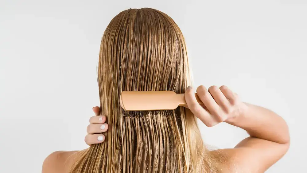 Woman brushing her wet, straight hair from behind.