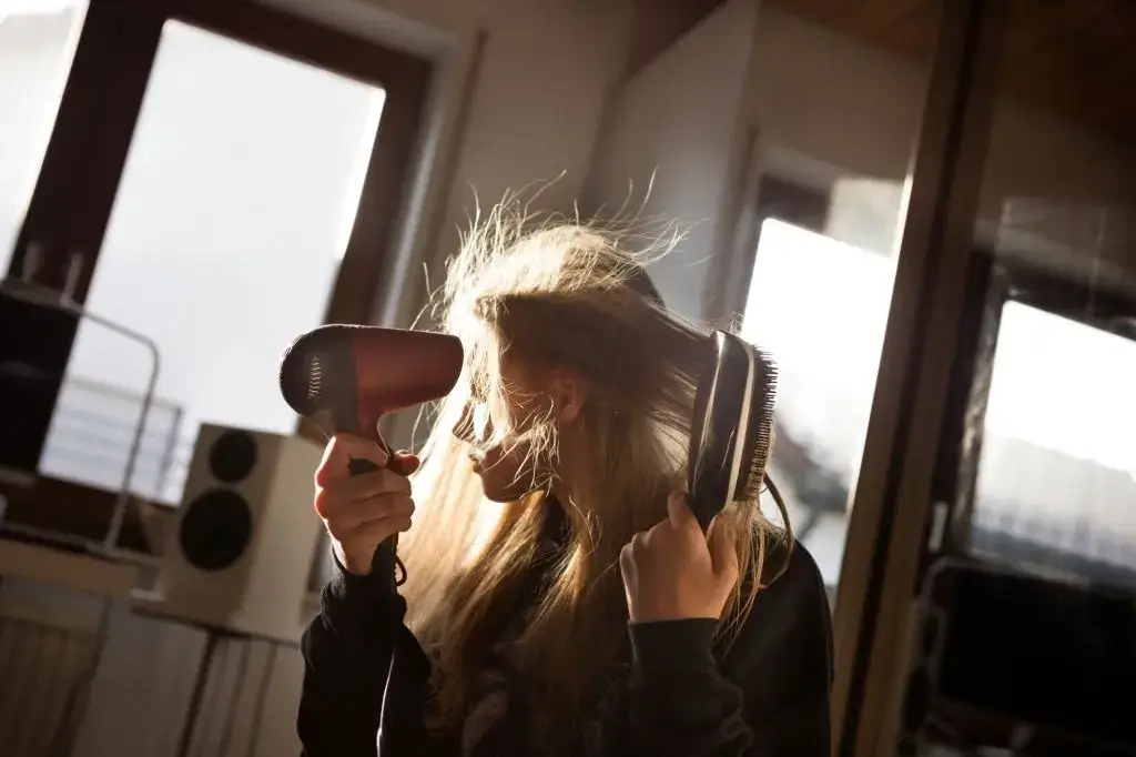 In the back light, a woman drying her hair with a hair dryer